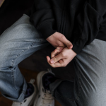 A young man in casual attire sitting with hands clasped, expressing contemplation.